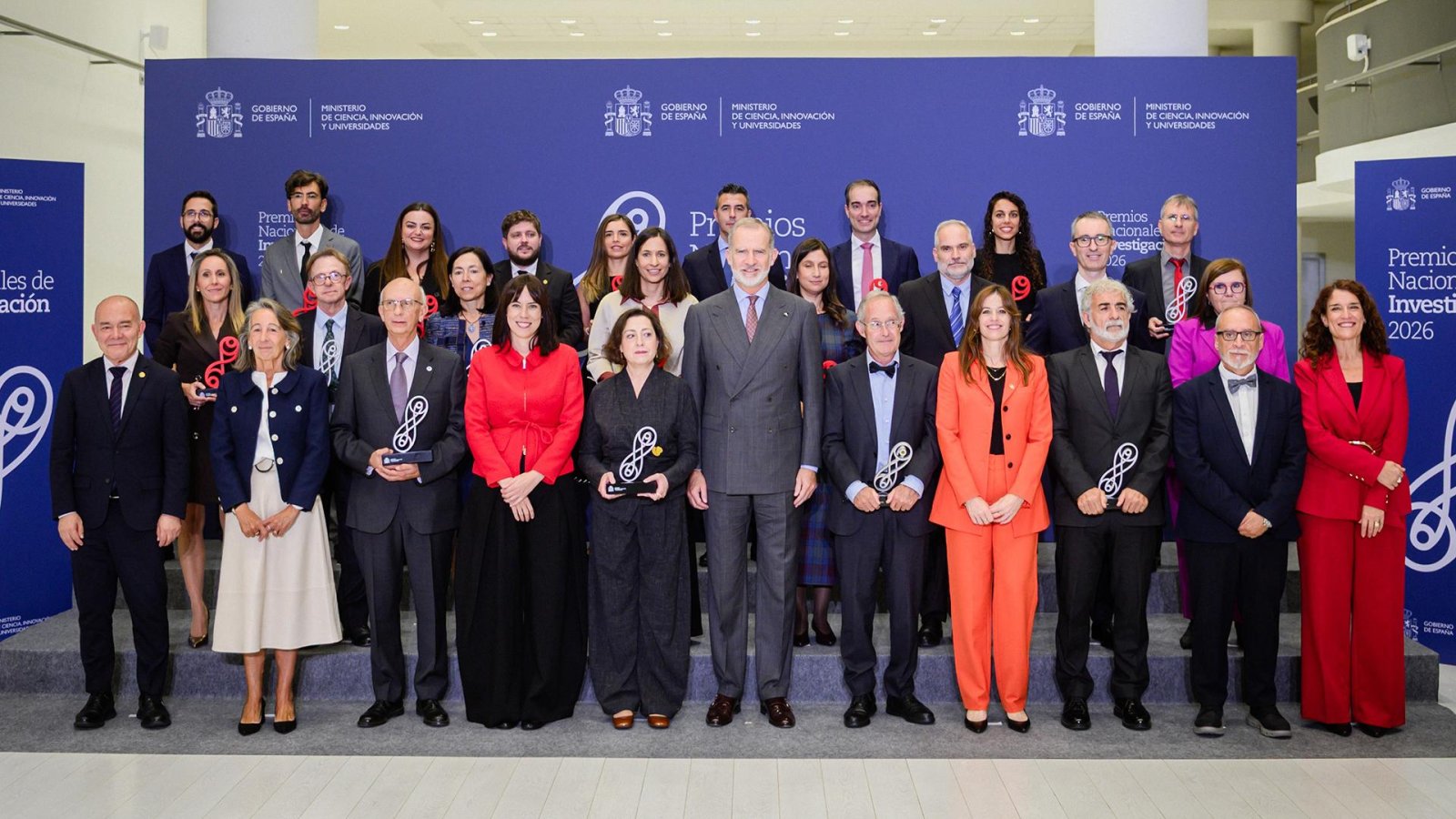 Un grupo de personas trajeadas posa en unas escaleras ante un panel azul con el escudo de España y el texto Premios Nacionales de Investigación.