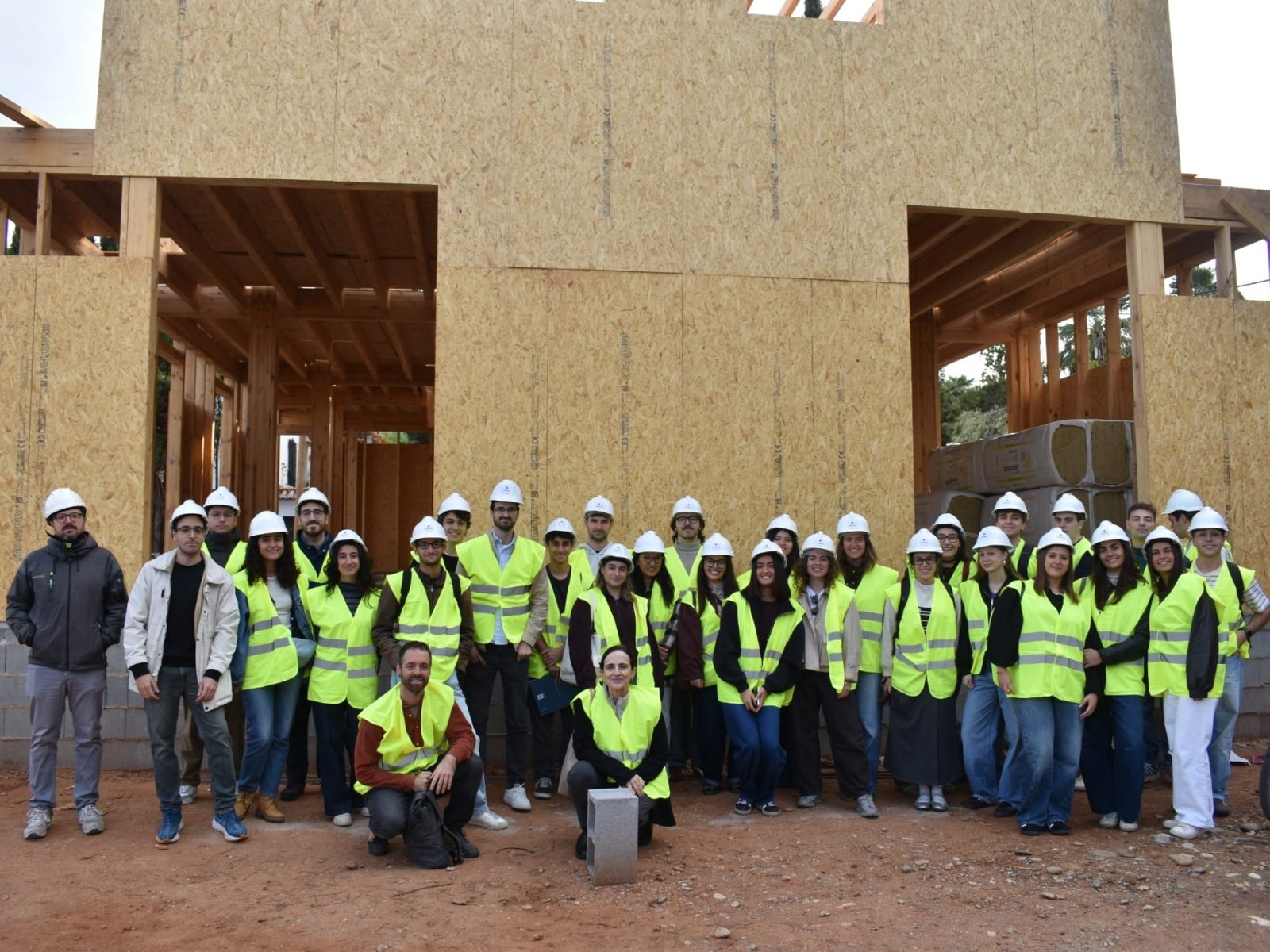 Un grupo de personas con cascos y chalecos reflectantes posa frente a una estructura de madera en construcción.