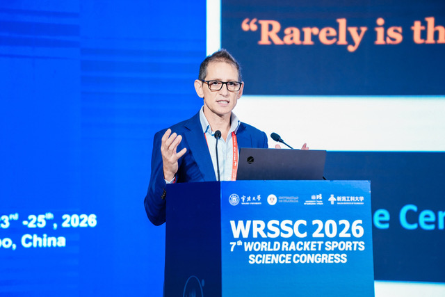 Un hombre con gafas y chaqueta azul habla ante un micrófono tras un atril con el cartel WRSSC 2026, sobre fondo azul.