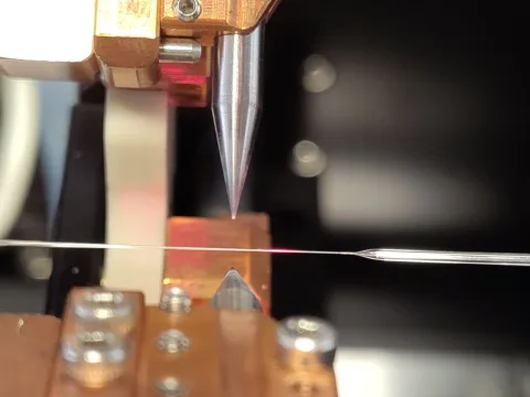 Una punta metálica cónica desciende sobre una fina fibra óptica sujeta en un soporte de laboratorio.
