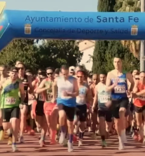 Corredores con dorsales avanzan por una calle bajo un arco azul con el texto Ayuntamiento de Santa Fe.